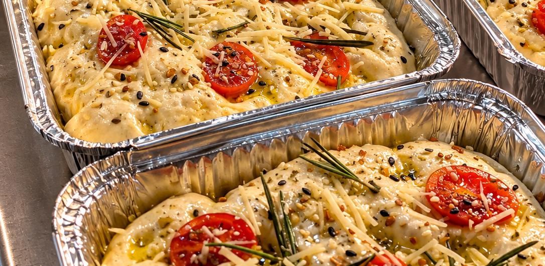 Focaccias en bandejas de aluminio con jitomate cherry, queso y romero